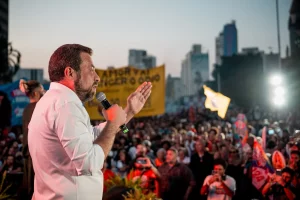 O candidato à prefeitura de São Paulo e ex-líder do MTST, Guilherme Boulos, fala em um microfone, à frente de uma multidão que acompanha seu comício eleitoral na Praça Roosevelt, em São Paulo.