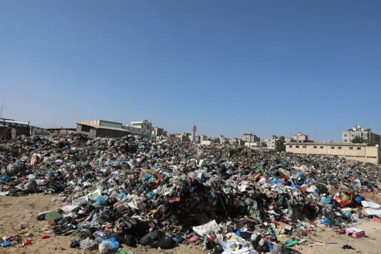 Montes de lixo se acumulam no chão, em um aterro sanitário improvisado na cidade de Gaza. No horizonte, o céu azul contrasta com a sujeira empilhada.